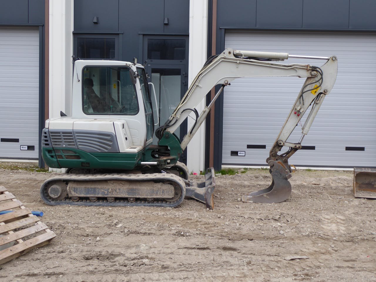 my-qualifications Side view of a compact excavator on a construction site in front of a building.
